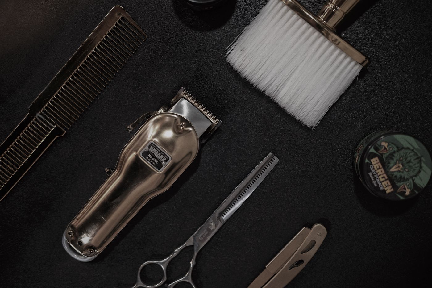 Clippers, scissors and barbering tools on a dark work surface